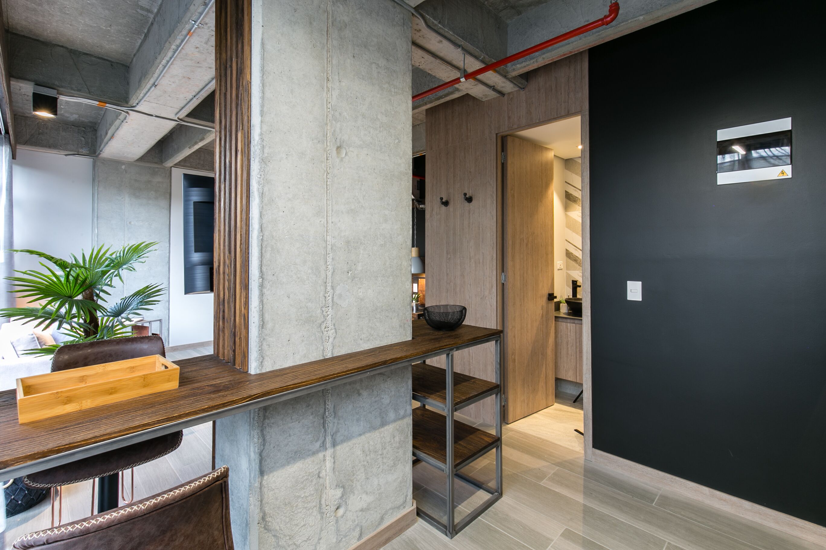 Un interior moderno con un pilar de concreto, una mesa de madera y una pared negra.
