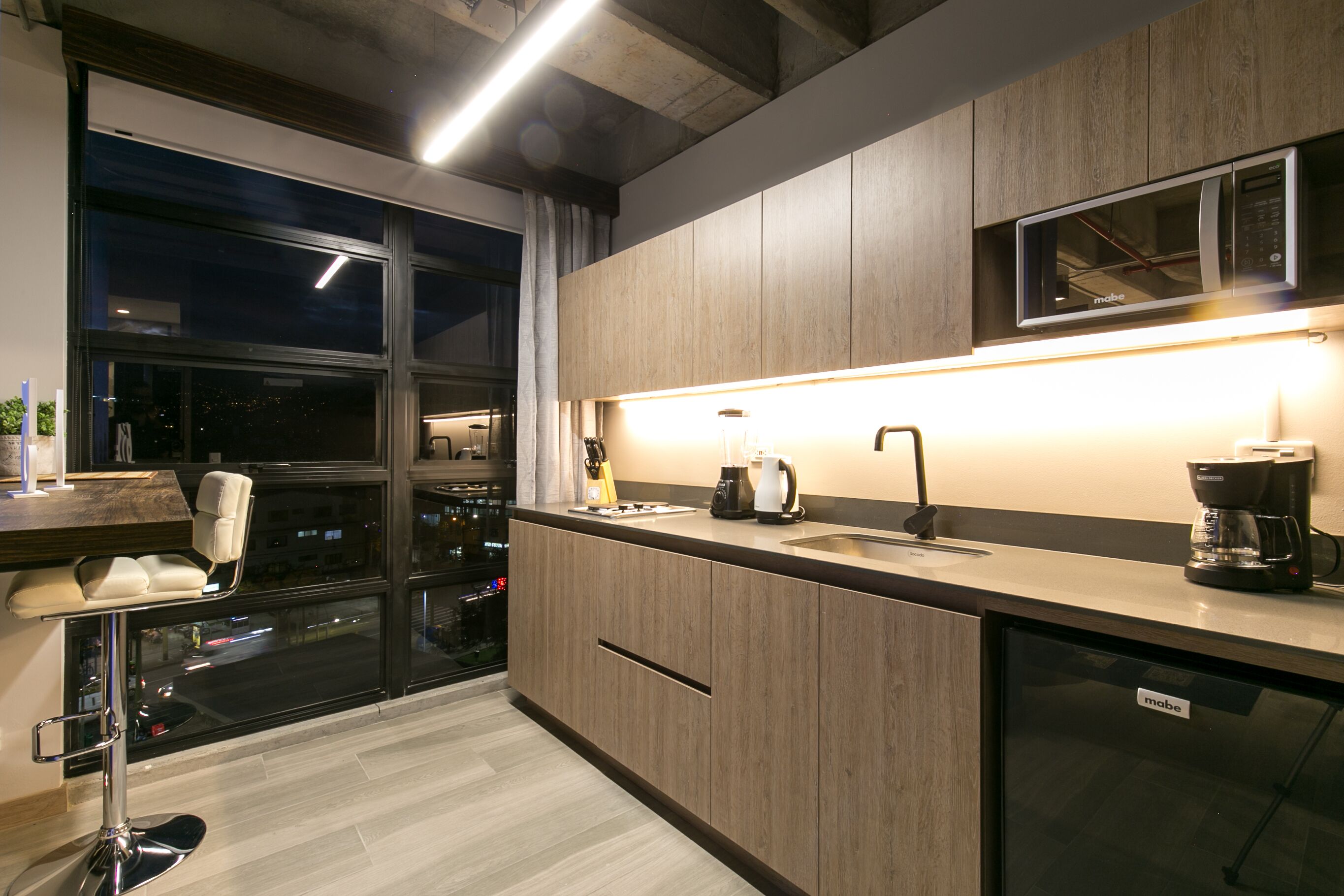 A modern kitchen with a large window, a bar stool, a coffee machine, and a microwave.
