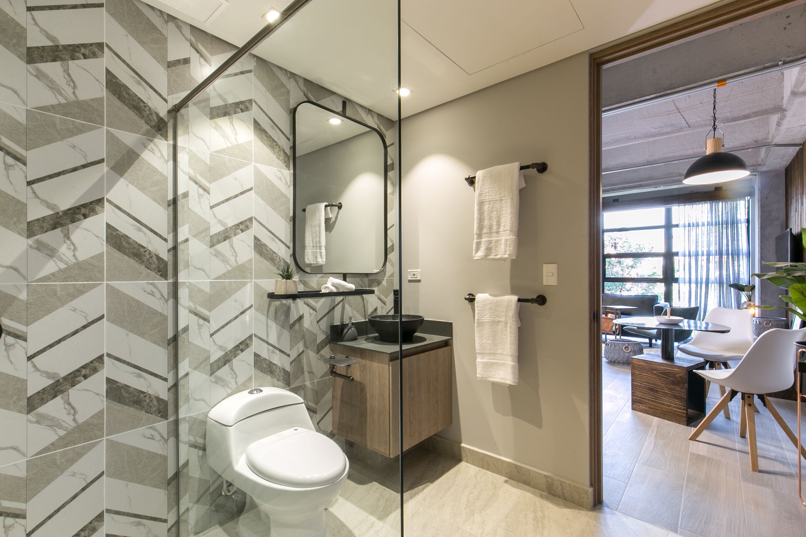 Un baño moderno con cabina de ducha de vidrio, pared con diseño de mármol, tocador de madera y vistas a una zona de estar exterior.
