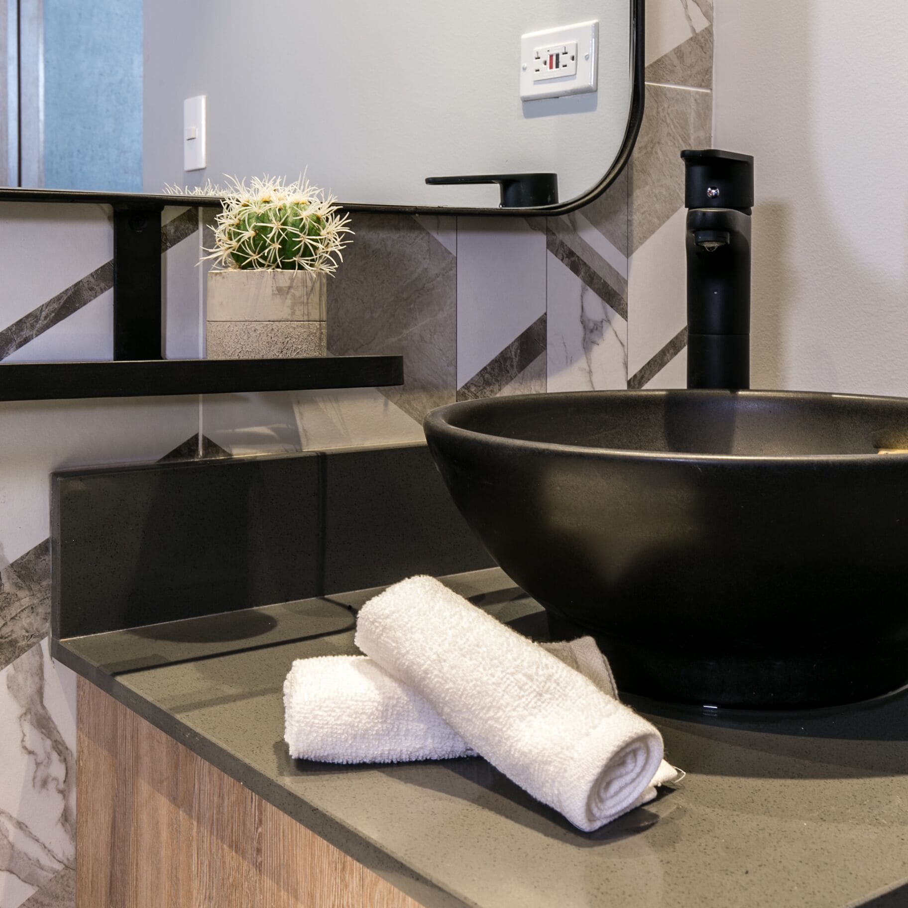 A modern bathroom with a black basin, a potted plant, and a towel on the counter.