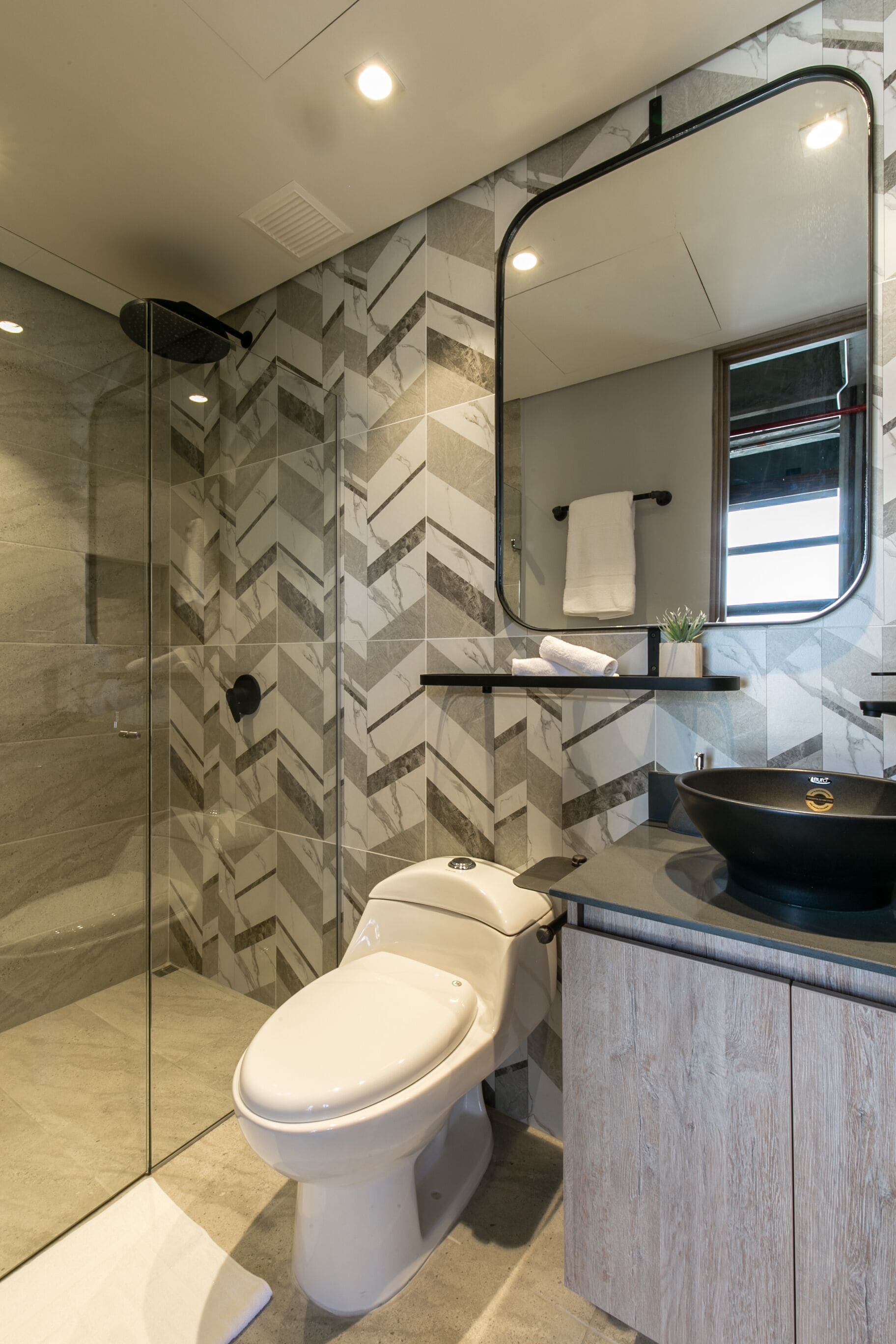 Une salle de bain moderne avec une douche à parois de verre, des toilettes blanches, un lavabo noir et un miroir au-dessus du lavabo.