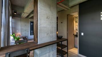 Een modern interieur met een betonnen accentmuur, een houten bank en een keukenruimte zichtbaar door een open deur.