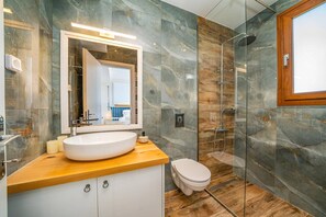 Een moderne badkamer met een grote spiegel, een rond wastafel, toilet en een douche met glazen wanden.