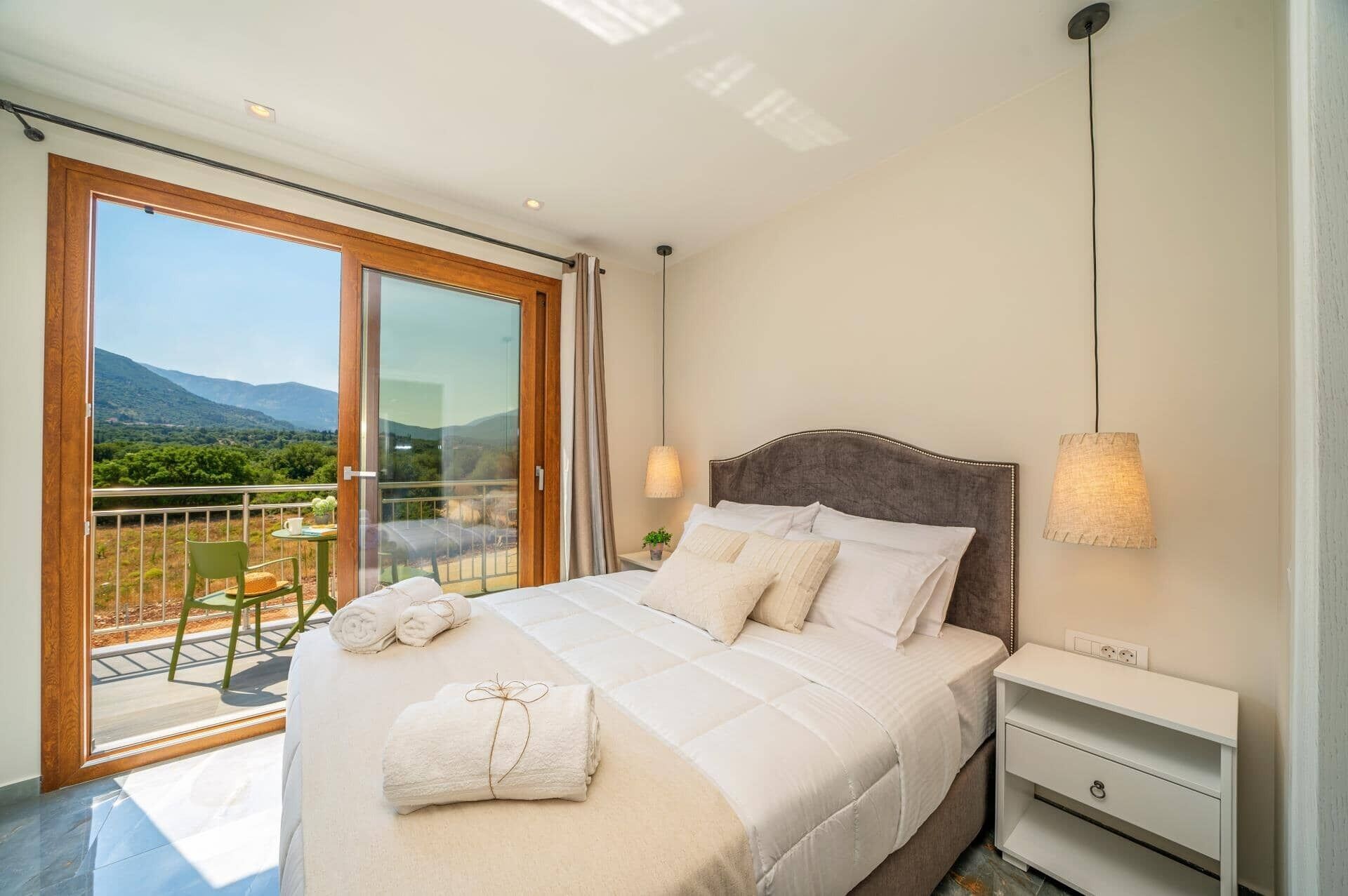 Un dormitorio con una cama grande, una mesita de noche, una lámpara y vistas a un balcón con sillas y una mesa.