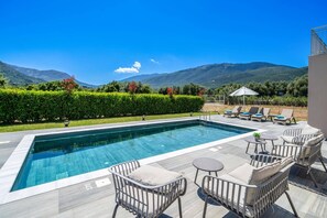 A swimming pool with lounge chairs and a view of mountains. - Villa Drogarati Retreat by Villa Plus (Cephalonia)