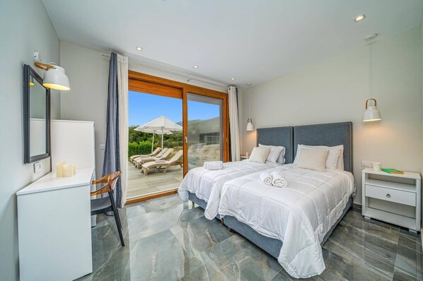 Een moderne slaapkamer met een groot bed, een bureau, een stoel en uitzicht op een zwembad.