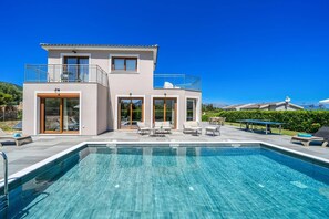A modern two-story house with a swimming pool, outdoor furniture, and a clear view of the mountains.