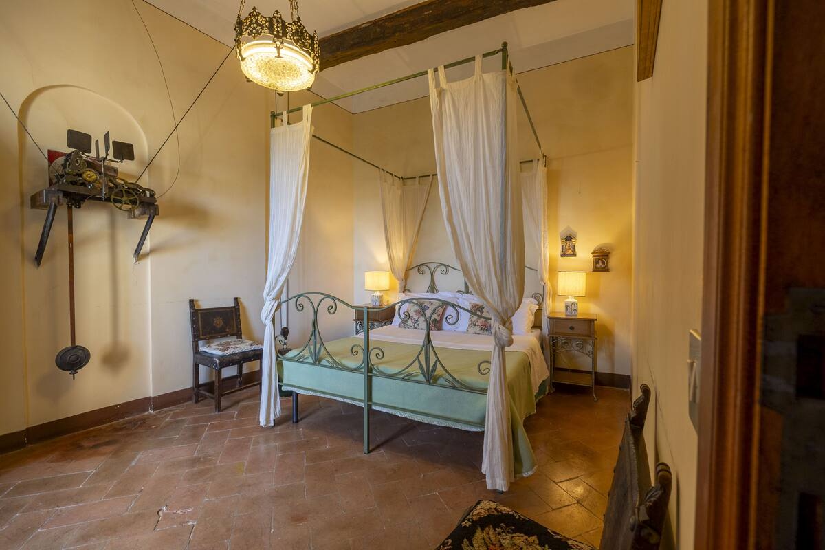 A four-poster bed with a canopy, a chair, a small table, and a wall-mounted clock.