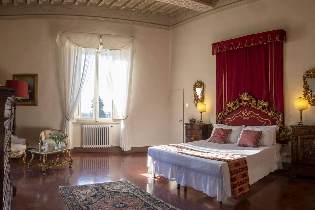 A classic bedroom with a large bed, ornate headboard, and a red curtain.