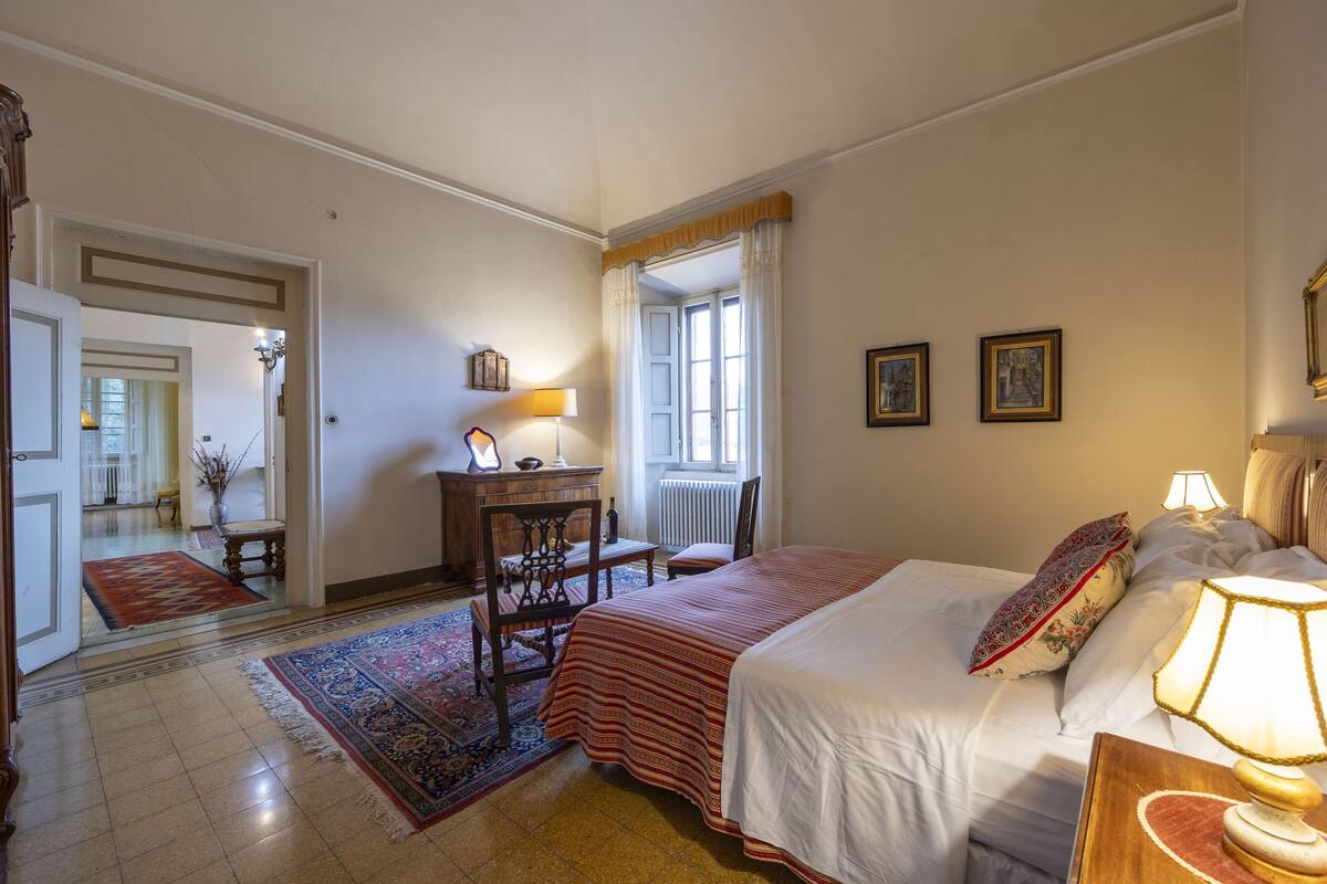 A bedroom with a bed, a desk, a chair, a lamp, and a window with curtains.