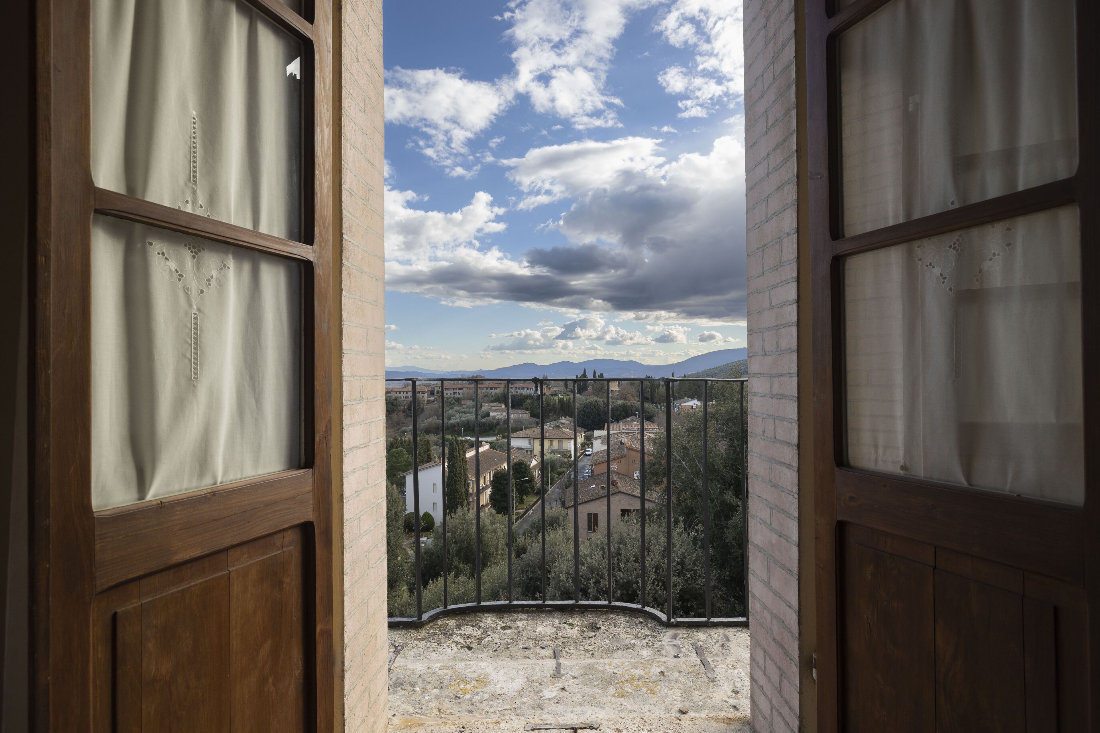 A view from a balcony with a metal railing, looking out over a residential area with houses and trees.