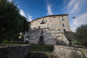 A historic stone building with a central arched entrance, multiple windows, and a balcony. - CASTELLO DI SOVICILLE- RESIDENZA D'EPOCA (Sovicille)
