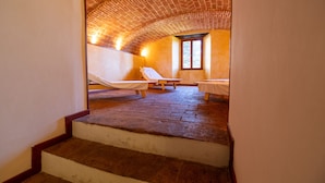 A spa room with a brick ceiling, two sunbeds, and a small table. - CASTELLO DI SOVICILLE- RESIDENZA D'EPOCA (Sovicille)