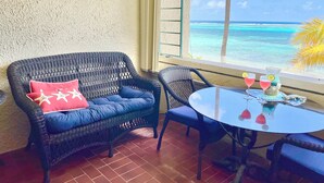 A wicker sofa with a red pillow and a glass table with drinks and a pitcher. - Beachfront Condo in Christiansted with Ocean View (Christiansted)