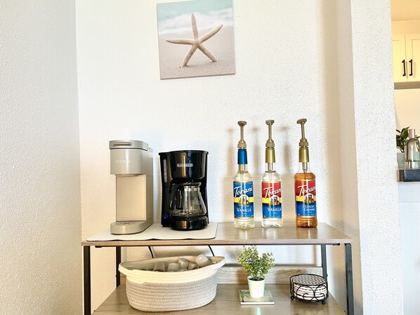 A kitchen counter with a coffee maker, a black coffee pot, and three Torani syrup bottles.