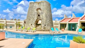 A swimming pool with lounge chairs, a stone tower, and a building with a red roof. - Beachfront Condo in Christiansted with Ocean View (Christiansted)