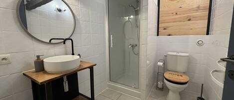 A bathroom with a wooden vanity, a round mirror, a toilet, and a glass-enclosed shower.