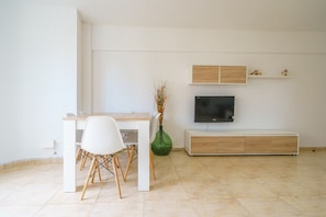 A modern living room with a wooden table, white chairs, a green vase, a flat-screen TV, and a built-in bench.