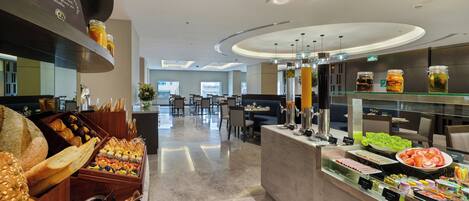 A modern hotel breakfast area with a variety of bread, pastries, and a juice bar.