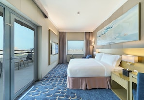Ein Hotelzimmer mit Bett, Schreibtisch, Stuhl, Fernseher und einem Balkon mit Blick auf die Stadt.