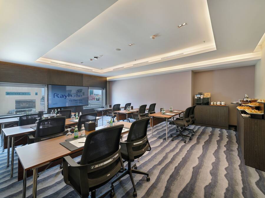 A conference room with multiple tables, chairs, a large screen, and a buffet area.