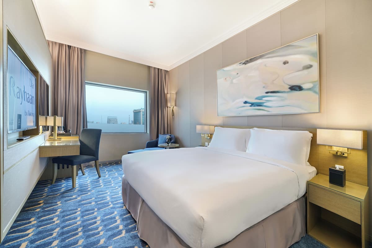 A hotel room with a large bed, a desk with a chair, a TV, and a painting on the wall.