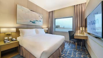 Habitación de hotel con una cama grande, un escritorio, una silla, televisión y vistas a la ciudad.