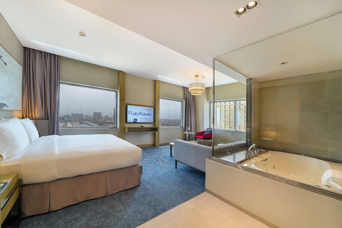 A hotel room with a large bed, a sitting area, a TV, and a bathtub.