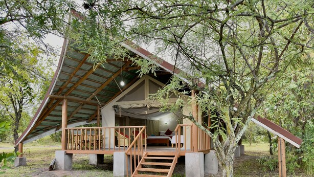 Une cabane rustique dotée d’une terrasse en bois, d’un escalier menant à une chambre en mezzanine et d’un petit espace porche.