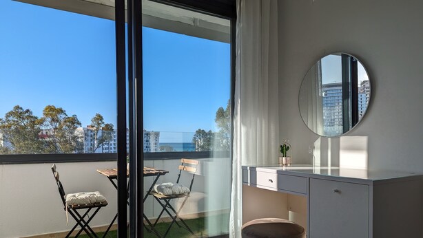 En moderne lejlighed med balkon, et rundt spejl, et træbord og en polstret stol.