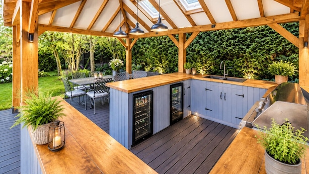 Una terraza de madera con cocina integrada, asientos exteriores y un pérgola con tragaluces.
