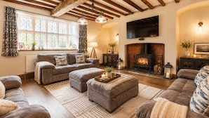 Una sala de estar acogedora con chimenea, vigas de madera y un ventanal con cortinas.