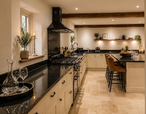 A modern kitchen with a central island, bar stools, a stove, and a black range hood.