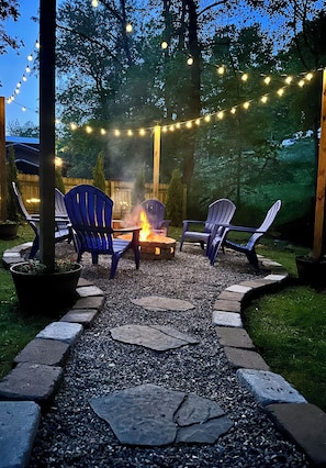 An outdoor seating area with Adirondack chairs, a fire pit, and string lights.