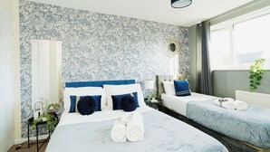 A hotel room with a marble-patterned wall, a large bed with two pillows, a bedside table with a lamp, and a window with curtains. - Canterbury Charm, Spacious 4 Bed House (Canterbury)