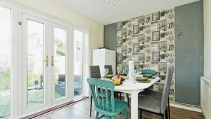 A dining area with a white table, teal chairs, and a stone-patterned wall. - Canterbury Charm, Spacious 4 Bed House (Canterbury)