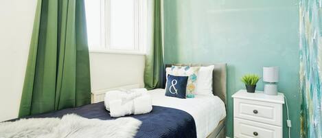 A neatly made bed with a fluffy white throw, a bedside lamp, and a nightstand with drawers.