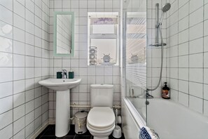 A small, white-tiled bathroom with a sink, toilet, and shower.