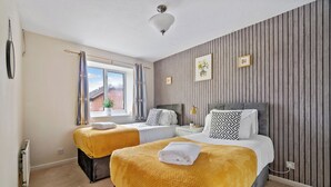 Quarto com duas camas, janela com cortinas, radiador e luminária fixada na parede.
