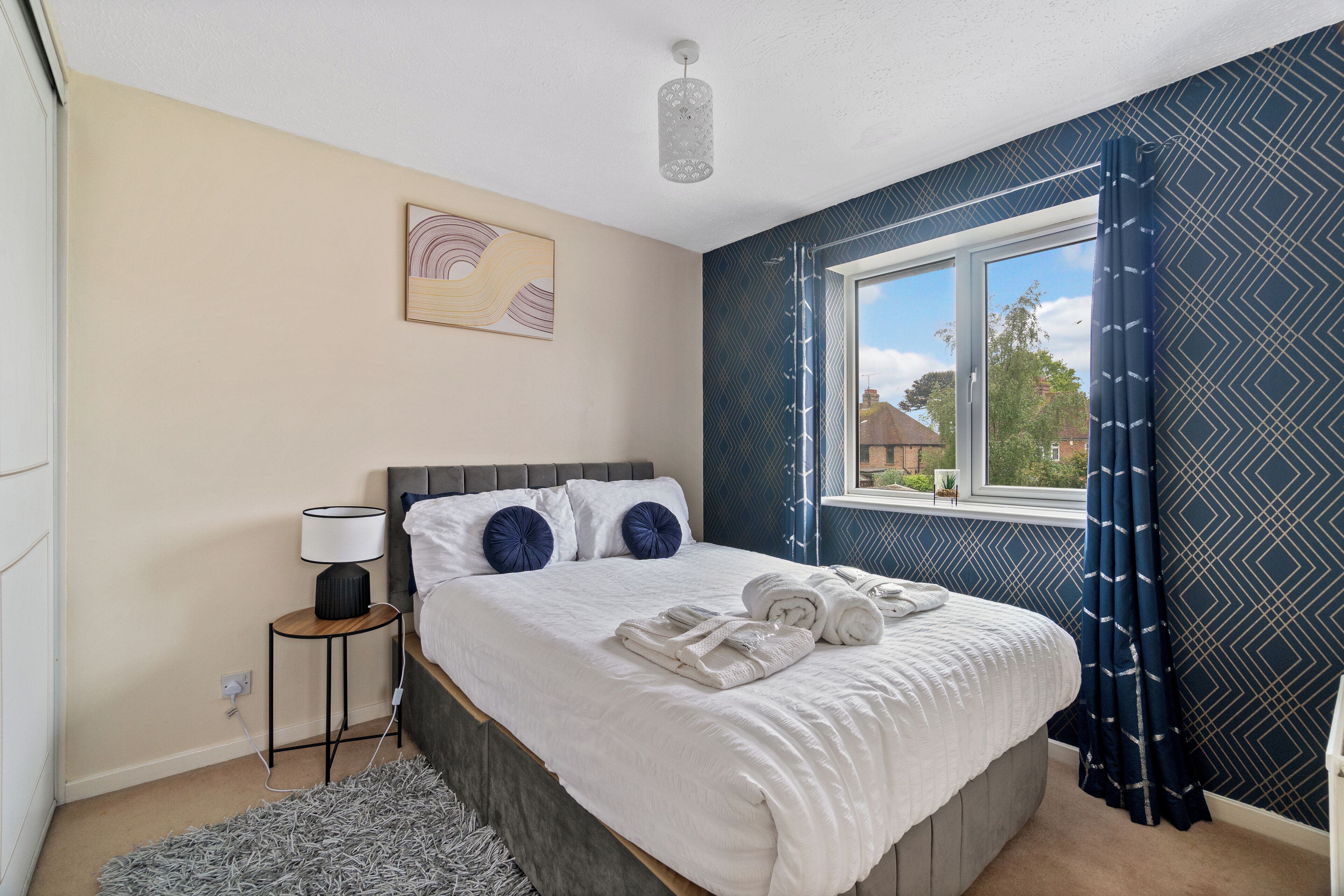 A bedroom with a bed, bedside lamp, and a window with curtains.