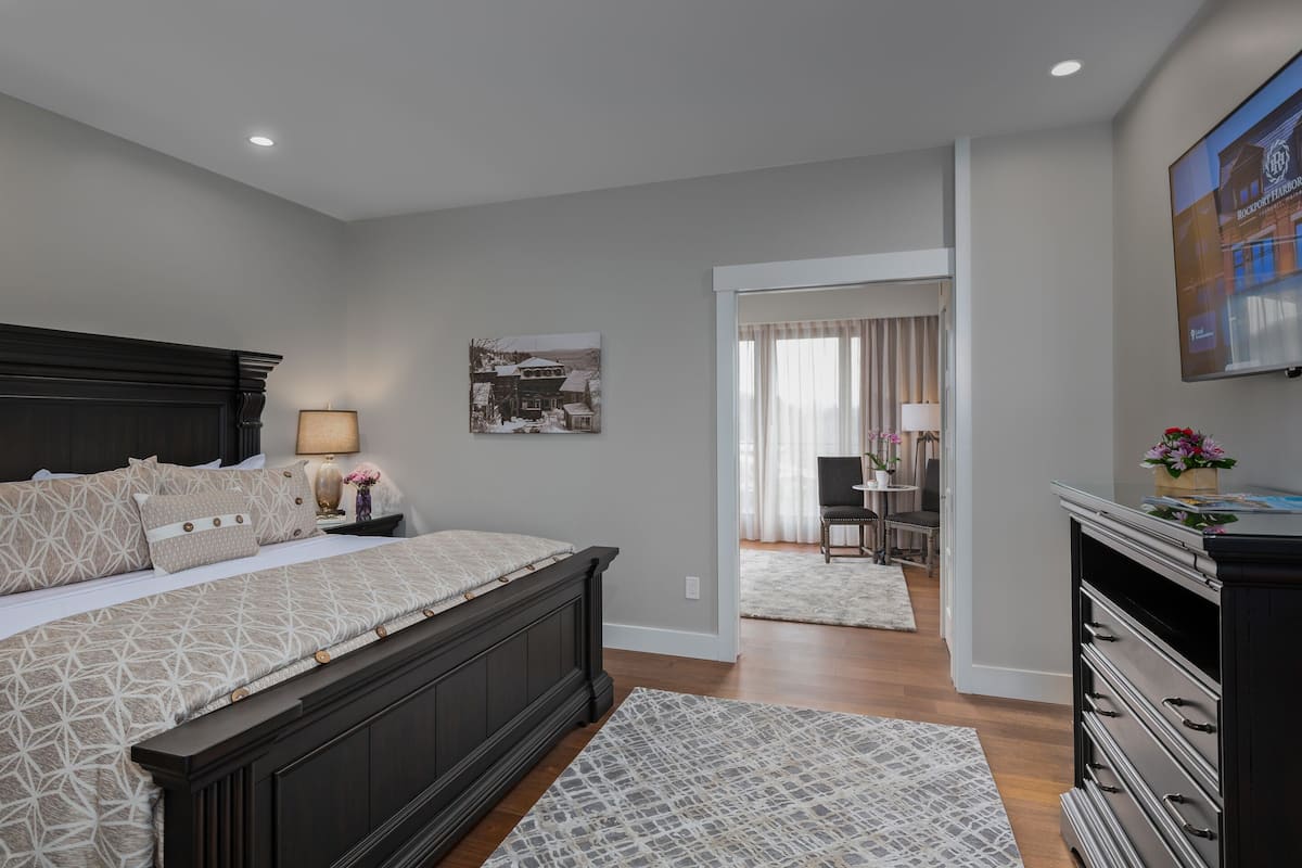 A bedroom with a bed, nightstands, a TV, and a view into another room.