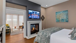 Un dormitorio con chimenea, una cama con ropa de cama estampada, un televisor colocado sobre la chimenea y un cuadro en la pared.