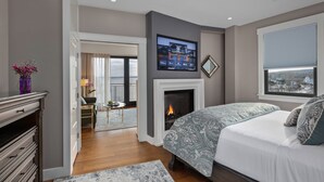 Una habitación de hotel moderna con chimenea, una cama con ropa de cama estampada, un televisor montado sobre la chimenea y vistas a la ciudad a través de una ventana.