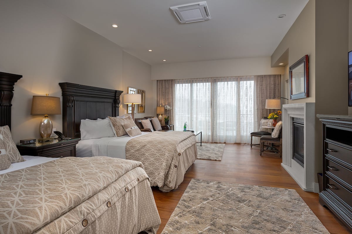 A spacious bedroom with two beds, a fireplace, and a large window with curtains.