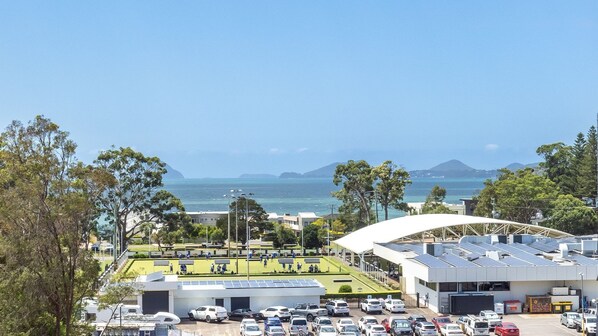 A parking lot with cars, a modern building with solar panels, and a view of the sea and mountains.