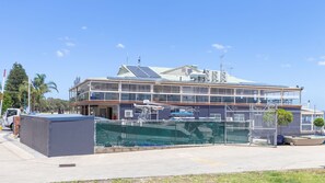 A multi-story building with a balcony, solar panels, and a fenced area with boats.