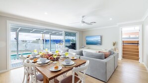 A modern living room with a dining area, a sofa, a TV, and a view of the sea.