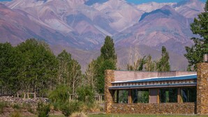 Un edificio moderno con pareti in pietra e ampie finestre, con montagne e cielo sereno sullo sfondo.