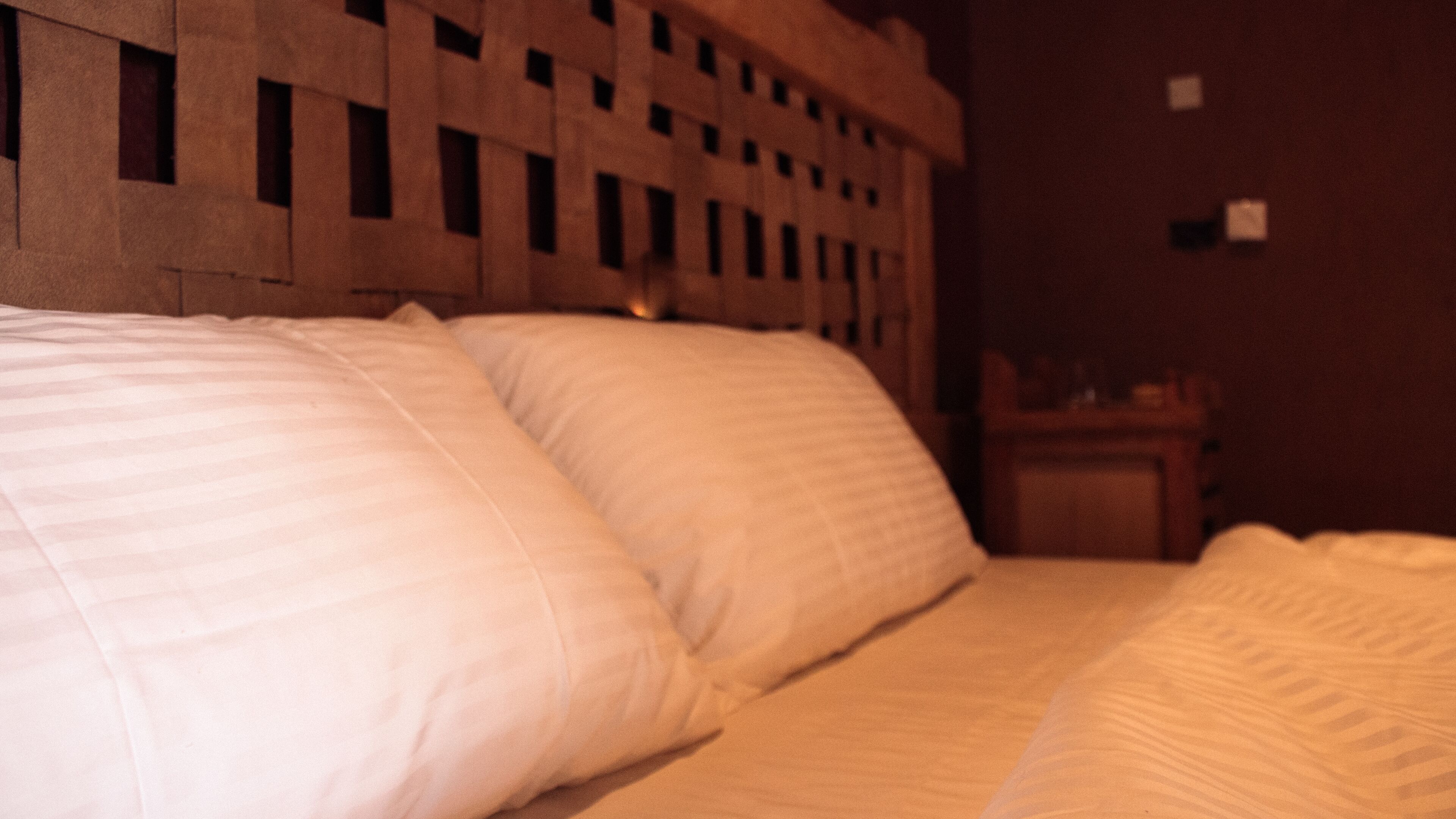 Una cama con ropa de cama blanca en una habitación con poca luz.