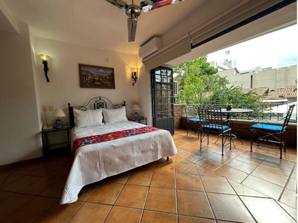 Une chambre à coucher comprenant un lit, une table de chevet, une lampe, un tableau et un balcon avec une table et des chaises.